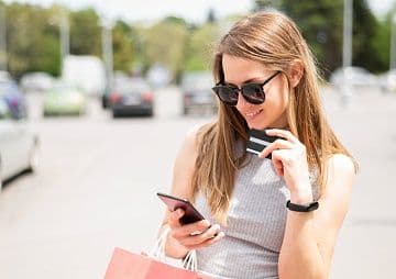 Красивая девушка сидит и смотрит в телефон в другой руке у нее пластиковая карточка